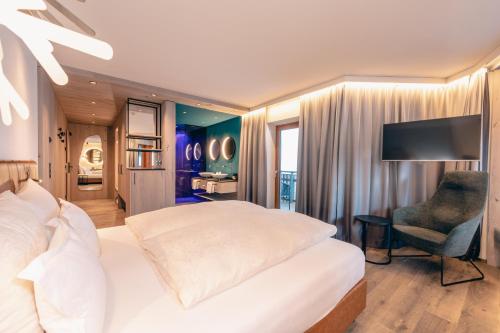 a bedroom with a bed and a chair and a television at ZillergrundRock Luxury Mountain Resort in Mayrhofen