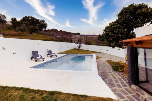 a swimming pool with two chairs next to a white wall at Pomar das Oliveiras - Private Swimming pool - Free EV Chrg - Pet Friendly in Carvalhal Cimeiro