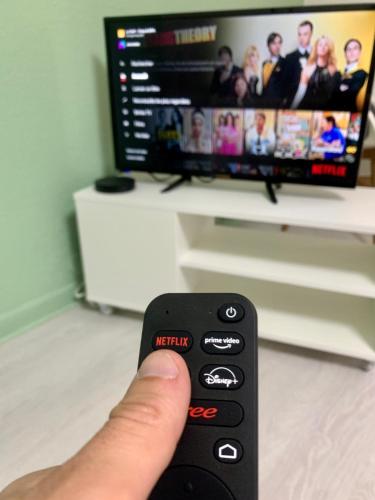 une personne tenant une télécommande devant une télévision dans l'établissement Le Golf Balnéo - Cosy & SPA - Appartement, à Saint-Étienne
