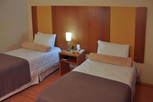 a hotel room with two beds and a table with a lamp at Cegil Hotel Boulevard in Resende