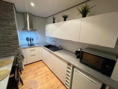 a kitchen with white cabinets and a black microwave at Casa Jaubertie - Appartement cosy et chaleureux refait à neuf - HYPER CENTRE BRIVE in Brive-la-Gaillarde