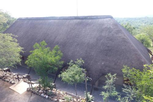 a thatch roofed house with trees and a bench at Balule Bushveld Safari Lodge in Phalaborwa