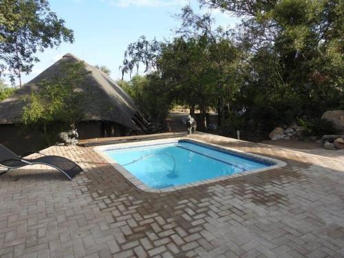 a swimming pool in front of a thatched house at Balule Bushveld Safari Lodge in Phalaborwa