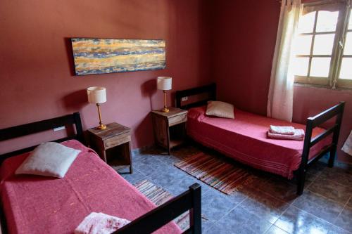 two beds in a room with red walls and a window at Los Abuelos Departamentos in Tafí del Valle