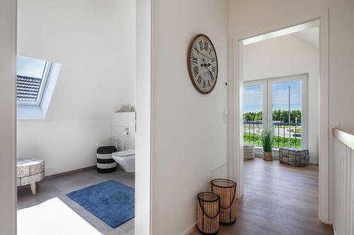 Ein weißes Zimmer mit einer Uhr an der Wand und einem Badezimmer. in der Unterkunft NordseeResort Büsum Ferienhaus 1 Beach House in Büsum