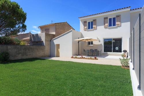 une maison blanche avec un parasol et une pelouse dans l'établissement Villa Lisa - piscine chauffée, à LʼIsle-sur-la-Sorgue