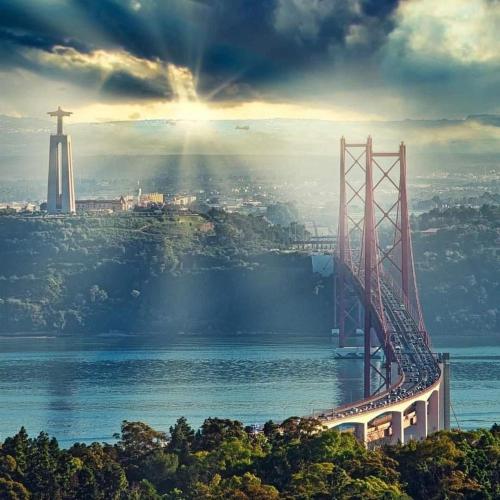 a bridge over a body of water with the sun shining at PALMA 3 BEDROOM APARTMENTS-a in Lisbon