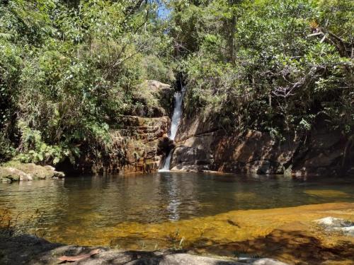 a person standing in the water in front of a waterfall at Bangalo a beira do rio em plena natureza in Petrópolis