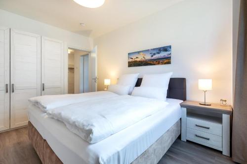 a bedroom with a large white bed and a night stand at Aparthotel Ostseeallee Aparthotel Ostseeallee 4-31 in Boltenhagen