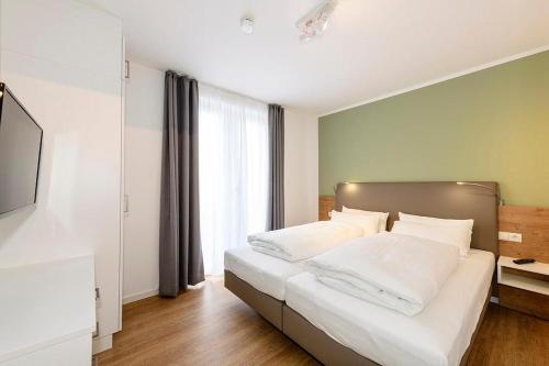 ein Schlafzimmer mit einem Bett mit weißer Bettwäsche und einem Fenster in der Unterkunft Deichhäuser Anna Küste Deichhäuser Anna Küste 1-30 in Bensersiel