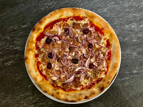 a pizza with onions on a plate on a table at Apparthotel Restaurant Steiners in Eben im Pongau