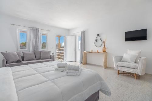 IL Vento Suites في مدينة ميكونوس: غرفة نوم بيضاء مع سرير أبيض كبير وأريكة
