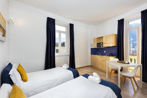 a room with two beds and a table and a kitchen at GuestHouse Lugano Center by LR in Lugano