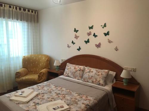 a bedroom with a bed and a chair and butterflies on the wall at Apartamentos turísticos CHUS in A Coruña