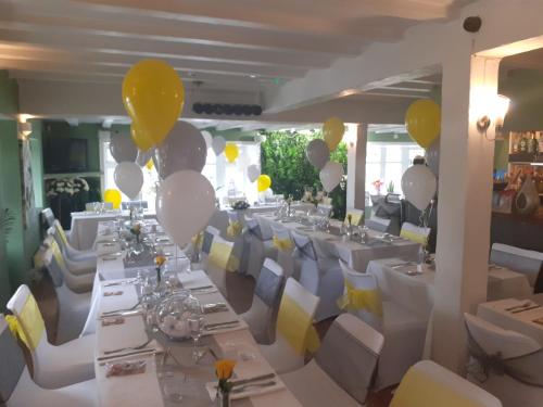 un salón de banquetes con mesas blancas y globos amarillos y blancos en The Balnoon Inn with rooms, en St Ives