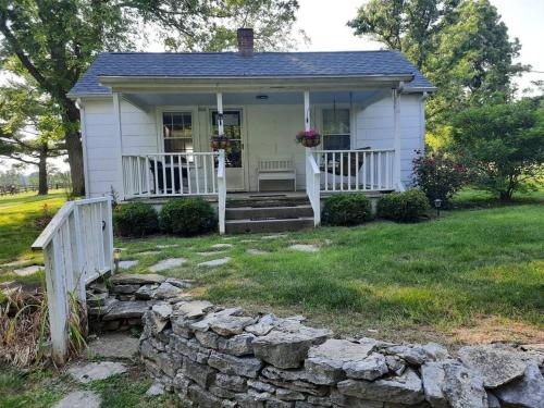 a small white house with a porch and a stone wall at Charming Cottage on a City Farm! in Lexington