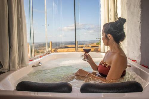a woman sitting in a bath tub with a glass of wine at Chalé Formoso - Chalé Romântico com Hidromassagem in Serra de São Bento