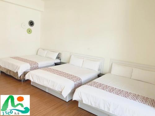 two beds in a room with white walls and wooden floors at 3520 Homestay in Taitung City