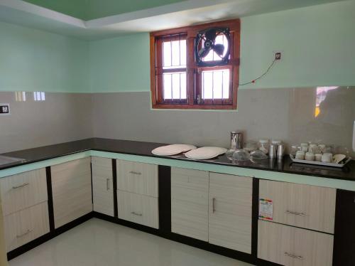 a kitchen with a counter with white cabinets and a window at MISBA HOMESTAY in Kodaikānāl