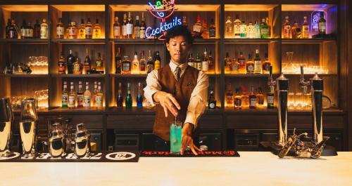 a man standing behind a bar with a drink at HOTEL SANSUI NAHA Ryukyu Onsen Naminoue-No-Yu in Naha