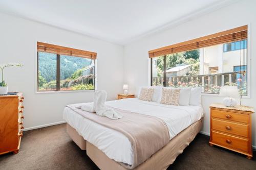 a white bedroom with a large bed and two windows at Town Centre Location with Stunning View - Unit 1 in Queenstown