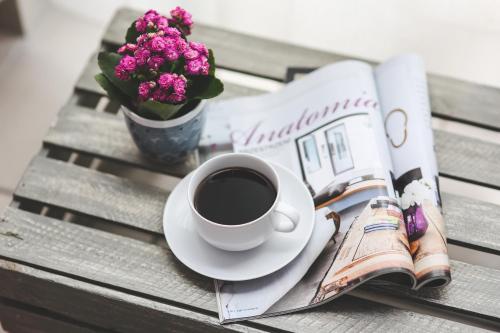 a cup of coffee and a newspaper on a table with a book and flowers at InStyle Aparthotel in St Julian's