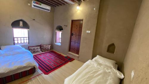 a bedroom with two beds and a door and a rug at Alqalah Inn in Al Ḩamrāʼ