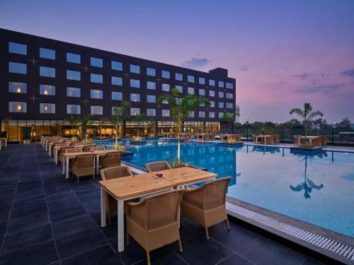 un hôtel avec une piscine dotée de tables et de chaises dans l'établissement Essentia Luxury Hotel Indore, à Indore