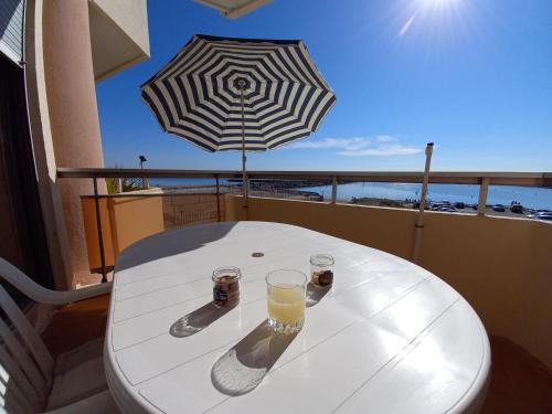 - une table avec deux verres et un parasol sur le balcon dans l'établissement Appartement vue mer / Carnon Plage, à Mauguio