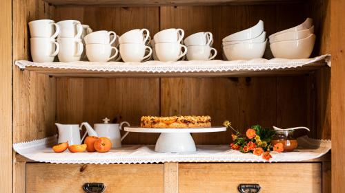 Un estante con tazas y platos y un pastel encima. en Natura Boutique Chalet Wellness SPA, en Dobbiaco