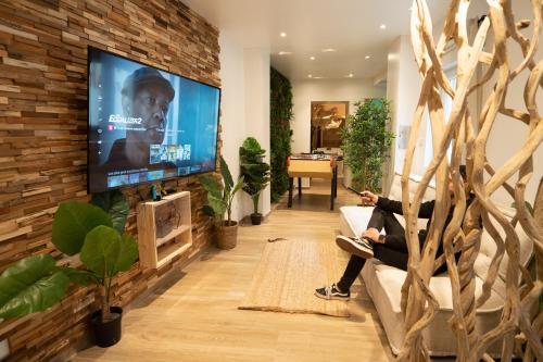 a person sitting on a couch in a living room with a tv at Capsule Thailande I Sauna I Balnéo I Console I jeux en bois I Cinéma I cour intérieure in Trith-Saint-Léger