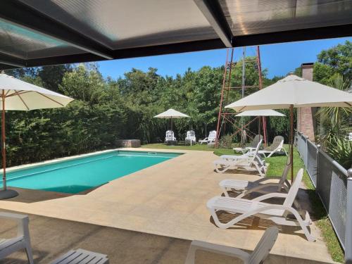 a swimming pool with white chairs and umbrellas at Descanso del Molino in Luján