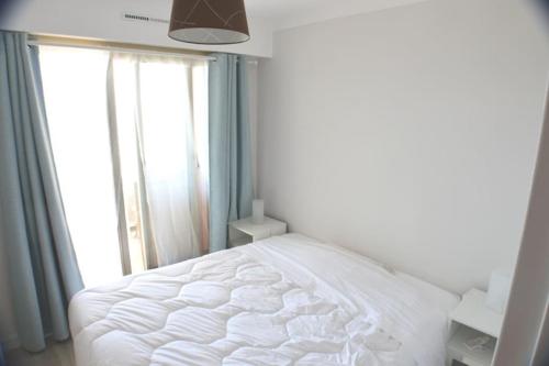 - un lit blanc dans une chambre avec fenêtre dans l'établissement 2 Piéces Clim Face a la plage vue Mer, à Cavalaire-sur-Mer