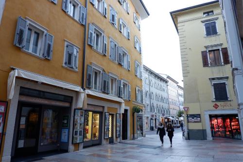 two people walking down a street next to buildings at MUROS - City Modern Living in Trento in Trento