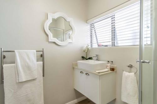 ein weißes Badezimmer mit Waschbecken und Spiegel in der Unterkunft C'estÇa Cottage Modern Luxurious Sounds of the Sea in Hermanus