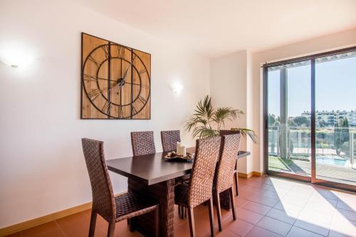 ein Esszimmer mit einem Tisch, Stühlen und einer Uhr in der Unterkunft Superbe appartement spacieux avec terrasse vue piscine in Vilamoura