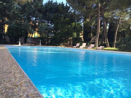 a blue swimming pool with chairs and trees at Cit'Hotel Le Mirage in Istres