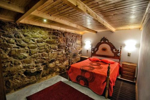 a bedroom with a red bed and a stone wall at Casa das Vinhas Camélias de BastoTurismo Rural in Celorico de Basto