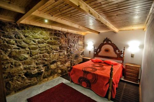 a bedroom with a red bed and a stone wall at Casa das Vinhas (Camélias de Basto-Turismo Rural) in Celorico de Basto