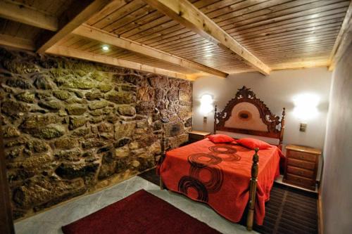 1 dormitorio con cama roja y pared de piedra en Casa das Vinhas Camélias de BastoTurismo Rural, en Celorico de Basto