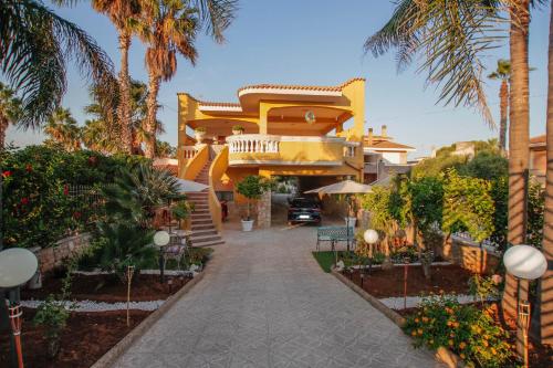a yellow house with palm trees and a driveway at Villa Silvana-Fronte Mare in Marsala