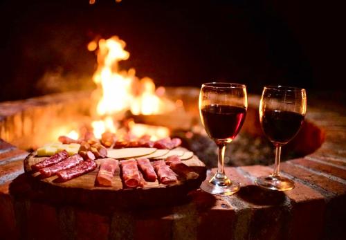 two glasses of wine and a plate of food next to a fire at Monteza Glamping in Piedecuesta