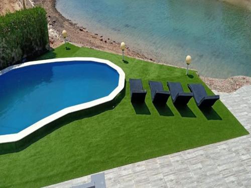 a swimming pool with four chairs on a grass field at Hurgadian Luxurious Villa Adan El Mamsha Long and Short Term in Hurghada