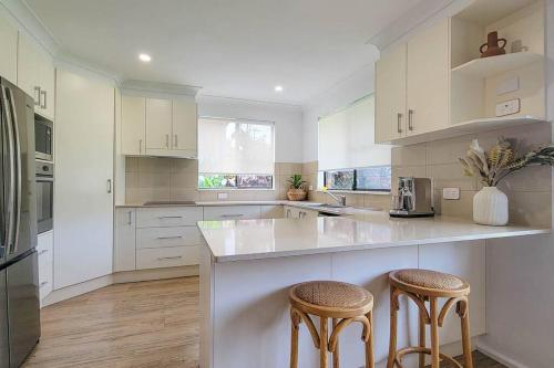 uma cozinha branca com dois bancos e um balcão em Coastal 3-bedroom home close by the beach em Port Macquarie