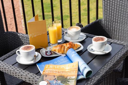 una mesa con dos tazas de café y un libro en The Imperial Hotel Exmouth, en Exmouth