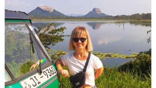 a woman standing in front of a van next to a lake at Woodsy Villa in Sigiriya