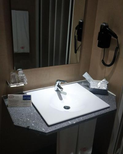 a bathroom counter with a white sink and a mirror at Hotel Comodoro in Corvo