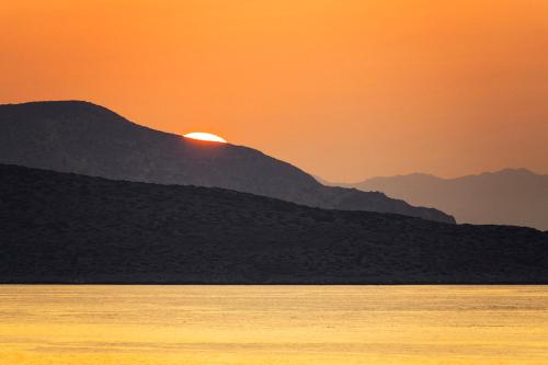 a sunset over the ocean with mountains in the background at Zefiros in Karavostasi