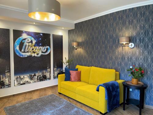 a yellow couch in a living room with a sign on the wall at Chicago Vendégház in Szentes