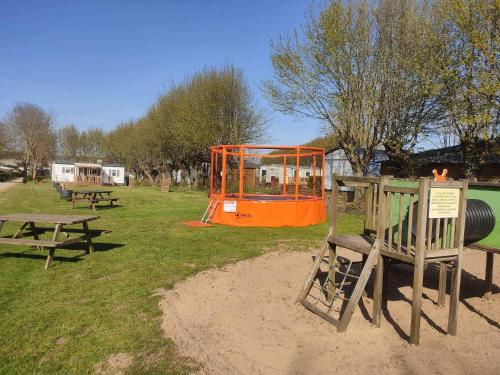 a park with two benches and an orange playground at Camping Les Sources Liencourt in Liencourt